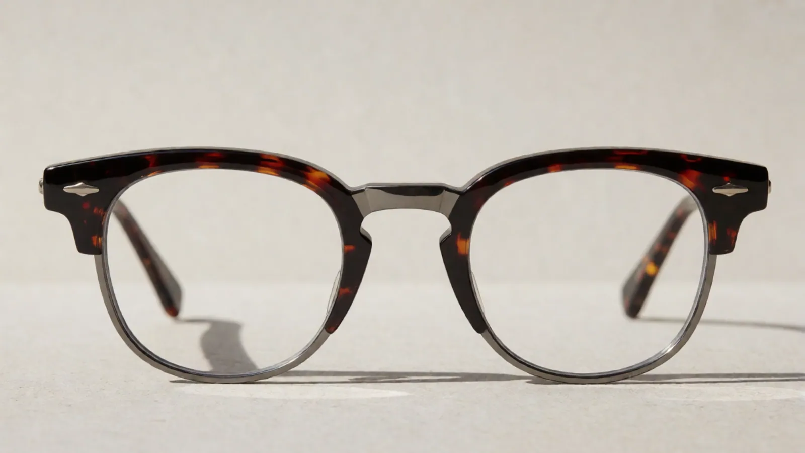The front of the tortoiseshell and gunmetal combination browline frame, photographed straight on against pale grey stone.