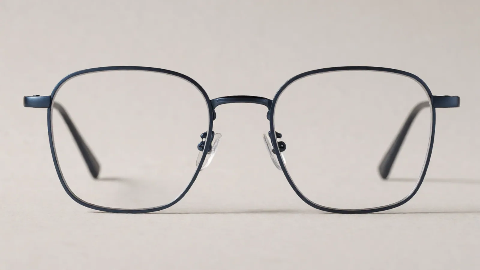 The front of the matte navy titanium square frame, photographed straight on against pale grey stone.