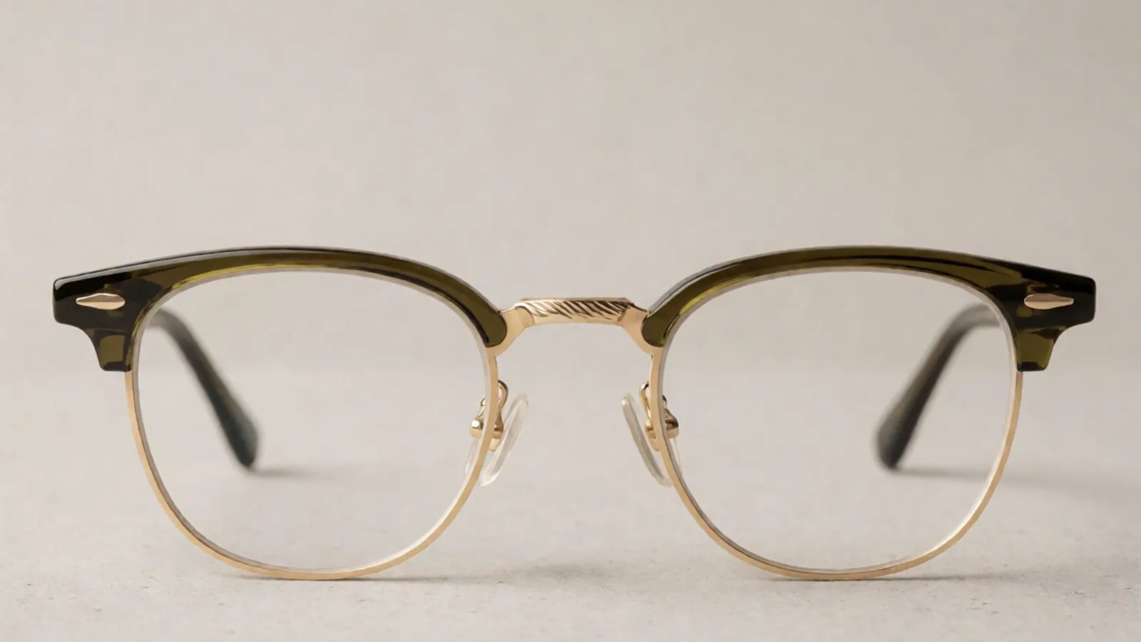 The front of the olive and brushed gold combination browline frame, photographed straight on against pale grey stone.