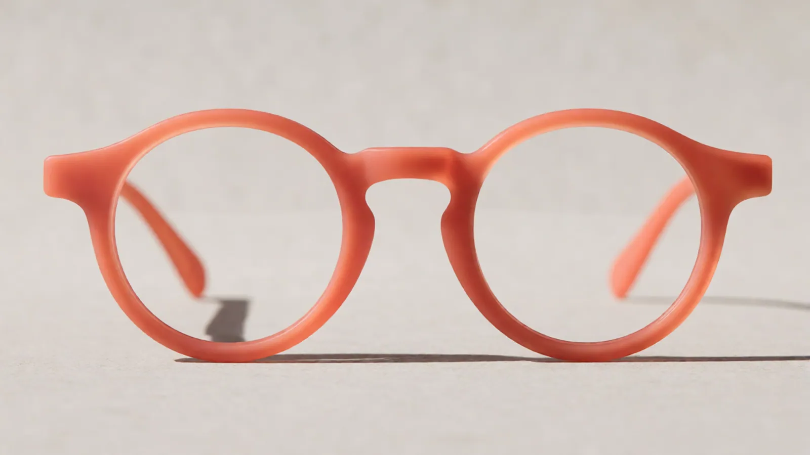 The front of the coral flexible nylon round frame, photographed straight on against pale grey stone.