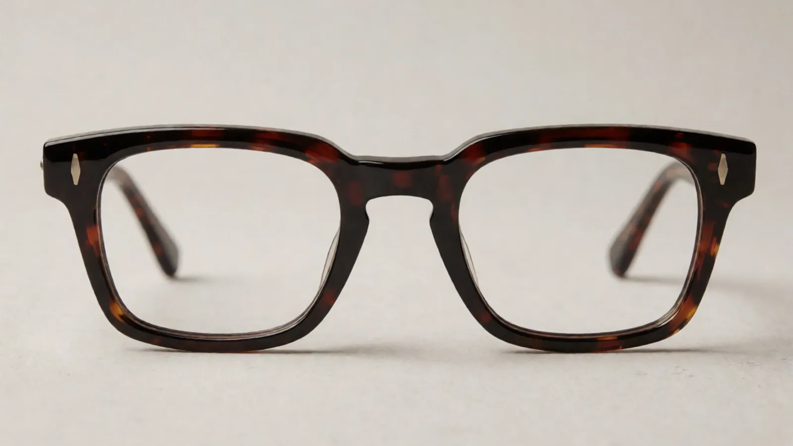 The front of the dark tortoiseshell acetate rectangle frame, photographed straight on against pale grey stone.