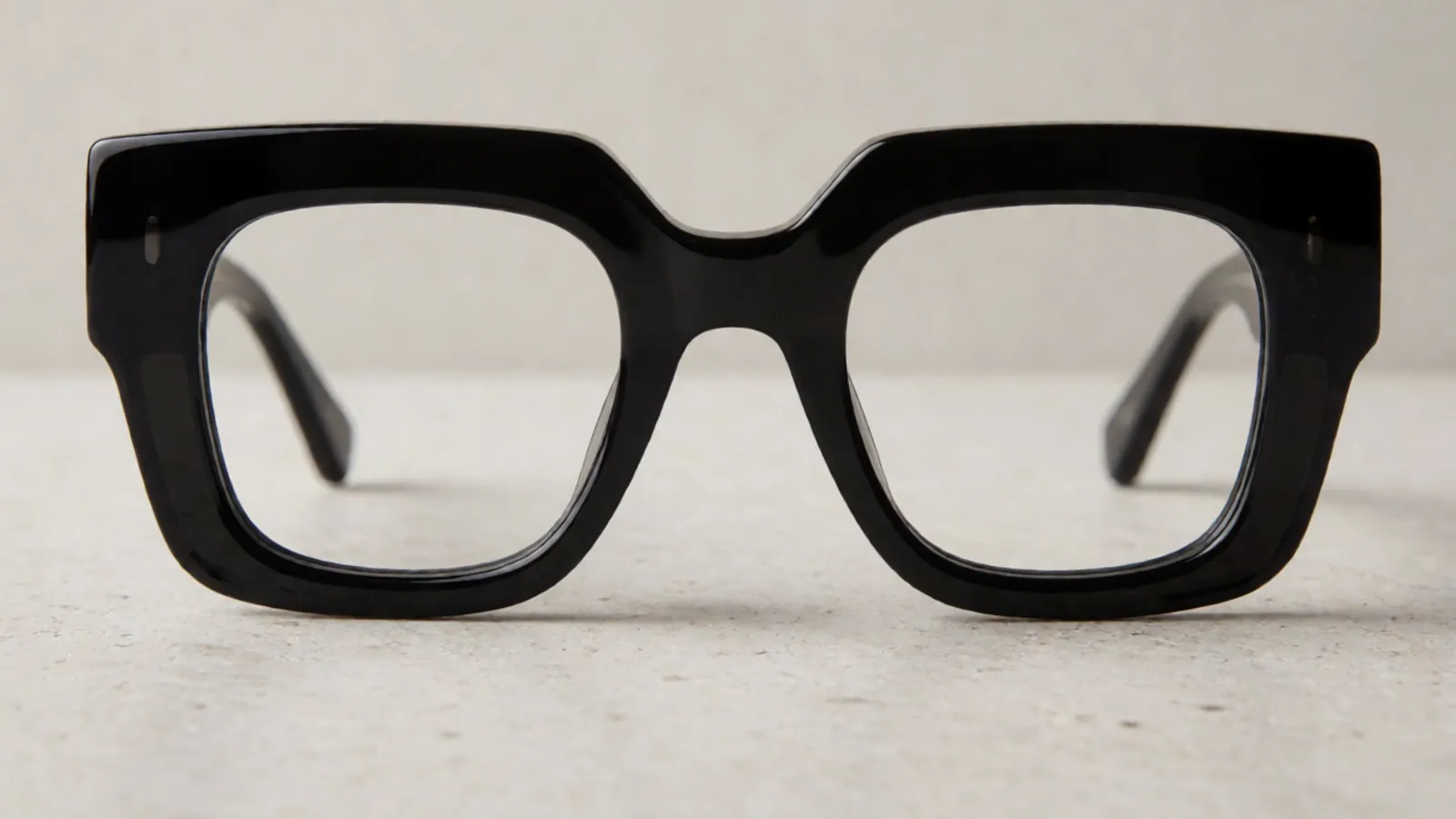 The front of the gloss black acetate square frame, photographed straight on against pale grey stone.