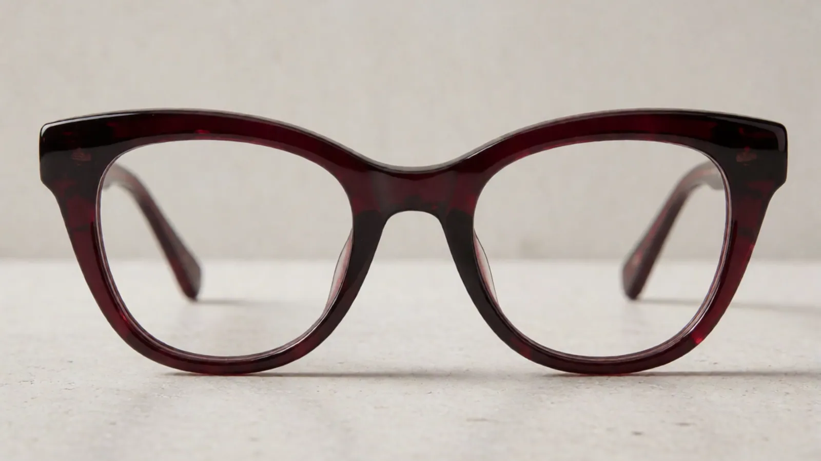 The front of the deep burgundy acetate cat-eye frame, photographed straight on against pale grey stone.